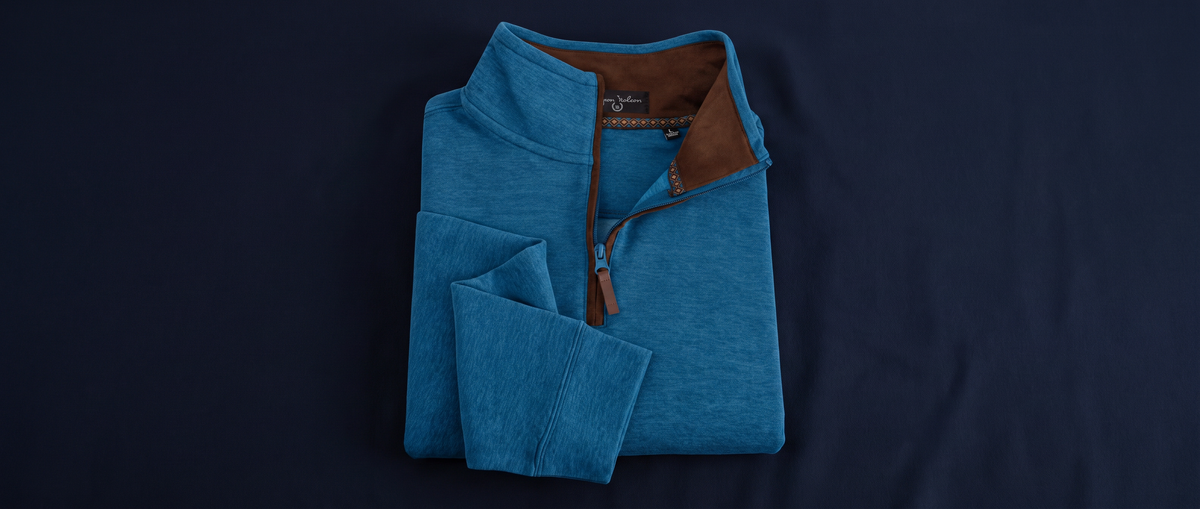 A folded blue quarter-zip pullover sweater with a brown collar lining, displayed on a dark navy background.