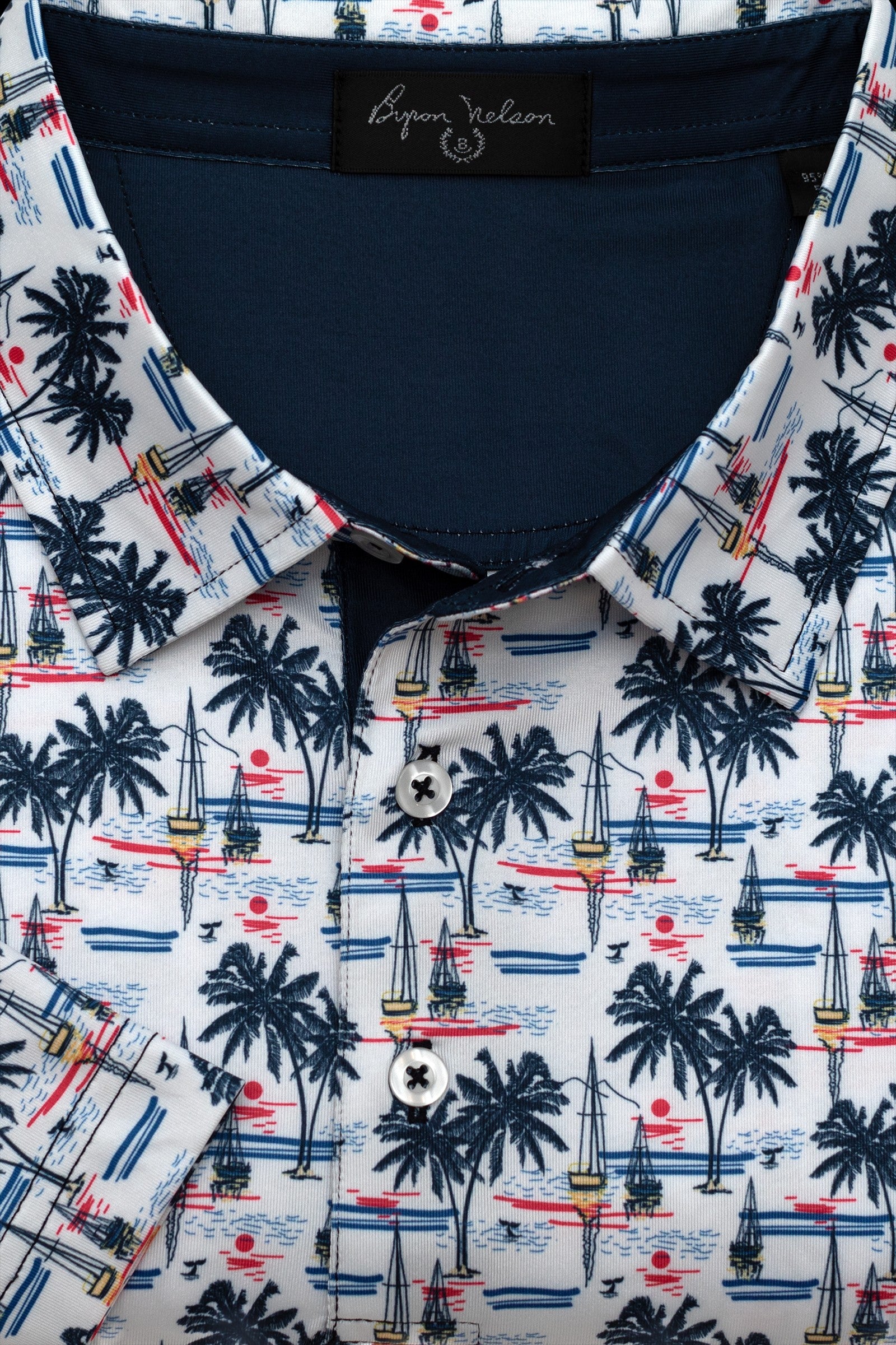 Byron Nelson white polo with all-over print of navy palm trees, sailboats, and red sunset. Moisture-wicking fabric.